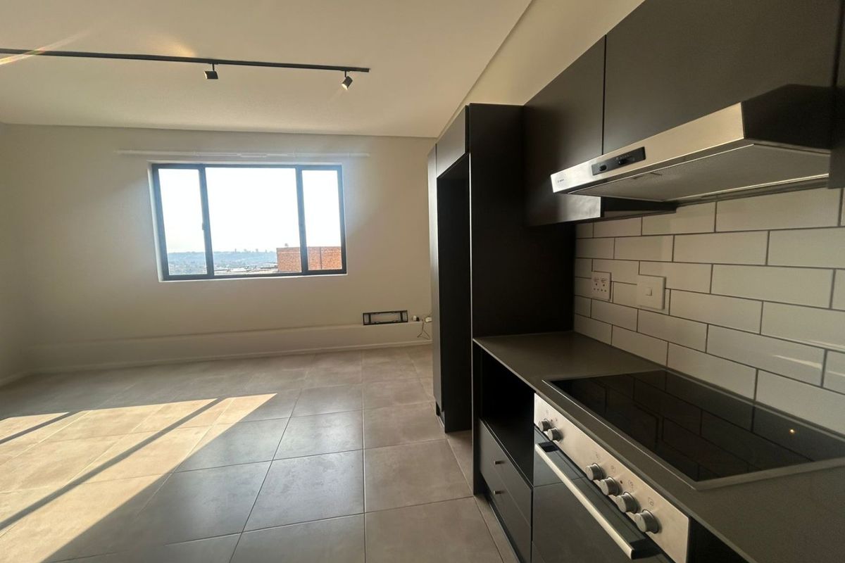 Modern open-plan kitchen and living area featuring dark cabinetry, integrated appliances, subway tile backsplash, and large windows with natural light.