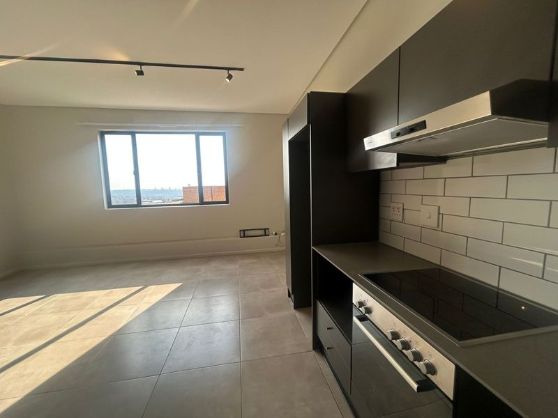 Modern open-plan kitchen and living area featuring dark cabinetry, integrated appliances, subway tile backsplash, and large windows with natural light.