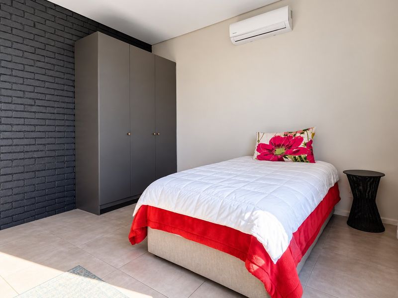 A well-maintained bedroom featuring a modern built-in wardrobe, a split-system air conditioner, and a stylish dark brick feature wall with neutral tiled flooring.