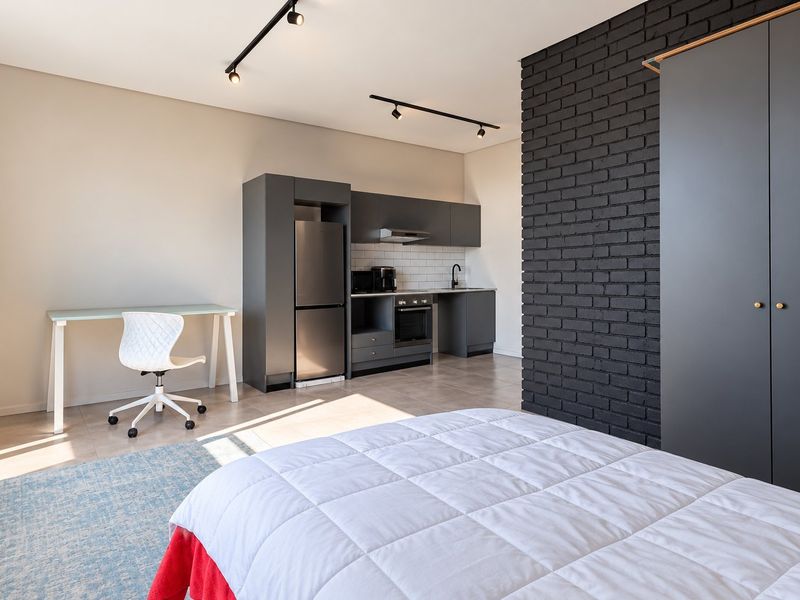 Modern open-plan studio apartment featuring a sleek kitchenette with built-in appliances, a striking black brick feature wall, and contemporary track lighting.
