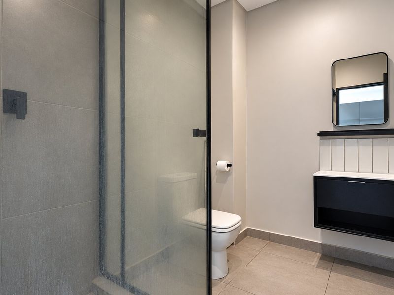 Modern bathroom featuring a glass-enclosed shower, wall-mounted vanity with black accents, and neutral floor-to-ceiling tiling.