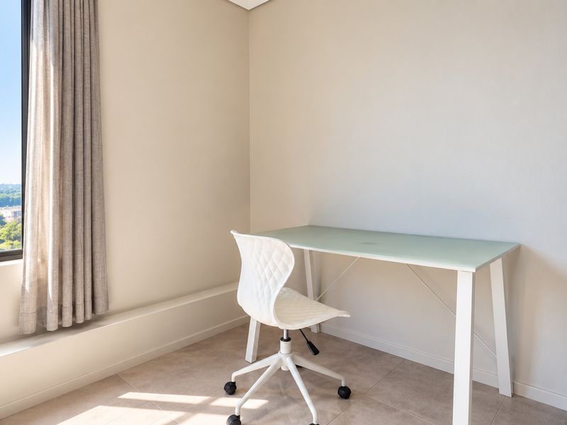 A bright, modern office space featuring neutral wall tones, tiled flooring, and a large window offering expansive city views.