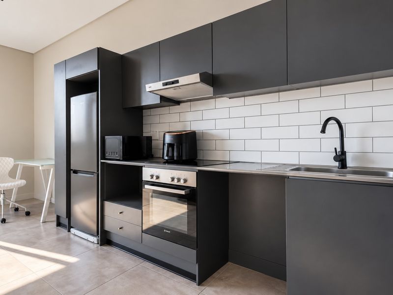 Modern kitchen featuring sleek dark cabinetry, subway tile backsplash, integrated stainless steel oven and hob, and a contemporary black mixer tap.