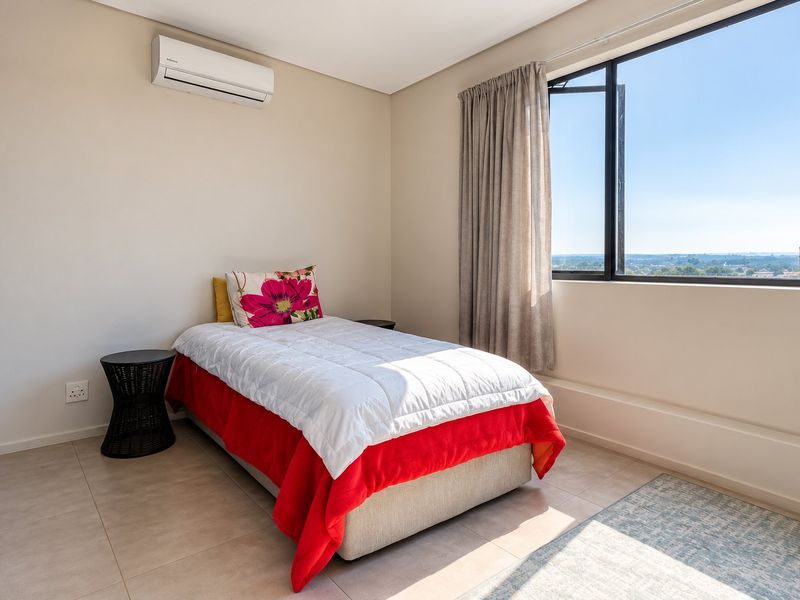 A bright and well-maintained bedroom featuring tiled flooring, a wall-mounted air conditioning unit, and a large window with natural light.
