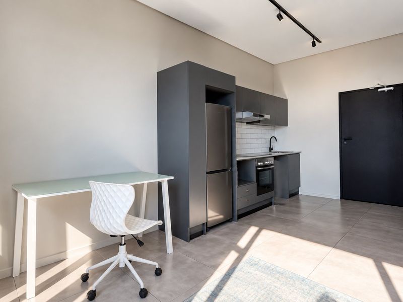 Modern open-plan kitchen area featuring sleek dark cabinetry, integrated appliances, subway tile backsplash, and contemporary track lighting in a well-maintained apartment setting.