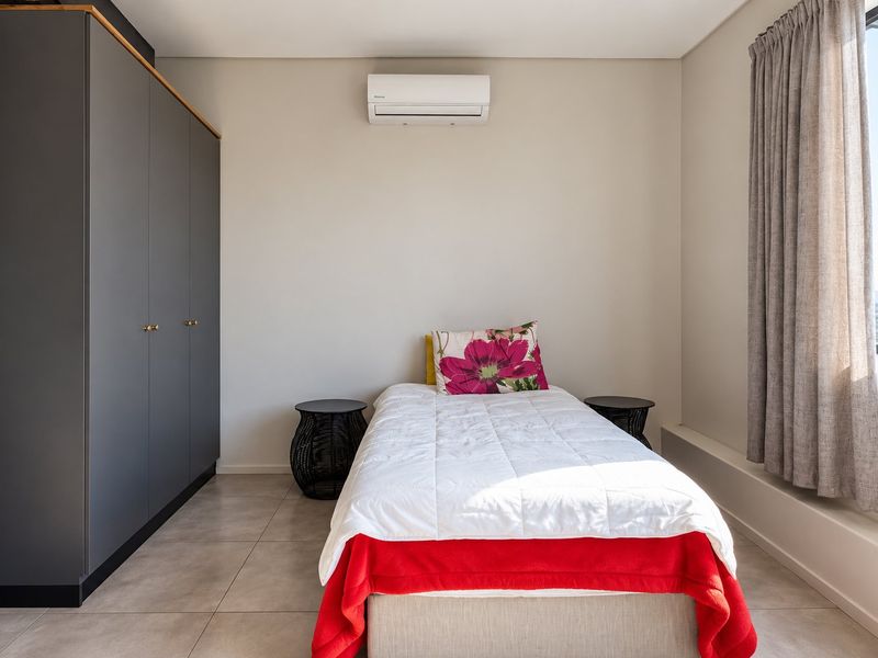 A modern bedroom featuring neutral tiled flooring, a large built-in wardrobe, and a wall-mounted split-system air conditioner.