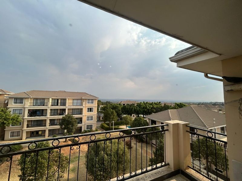 A spacious balcony featuring a wrought iron balustrade and tiled flooring, offering elevated views of the surrounding residential complex and landscape.