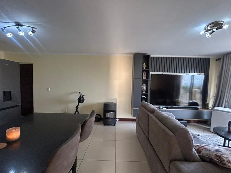 Open plan living area featuring large format floor tiles, a modern built-in media unit with slatted feature wall, and integrated ceiling lighting.