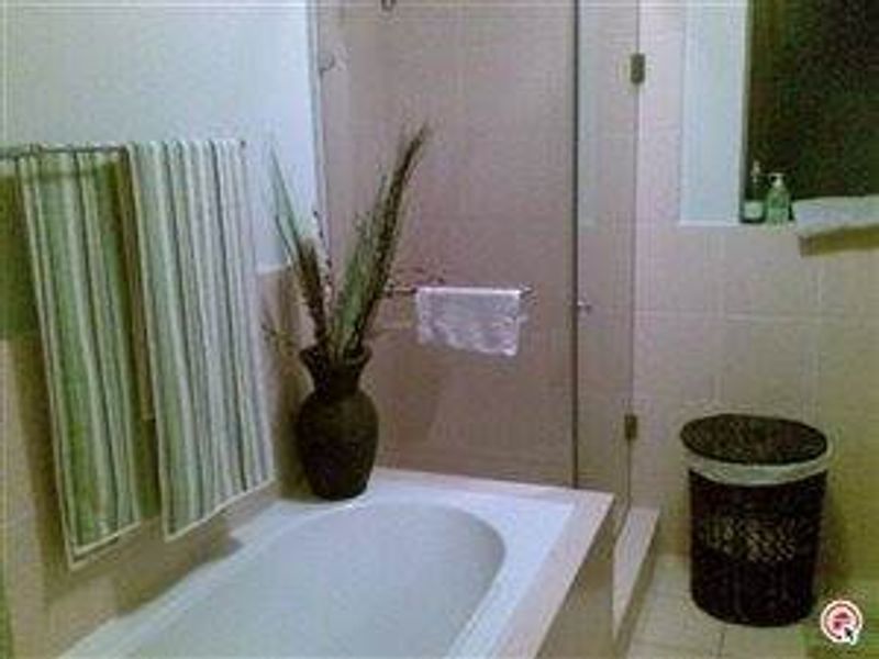 A functional bathroom featuring a built-in bathtub, a glass-enclosed shower, and neutral wall tiling.