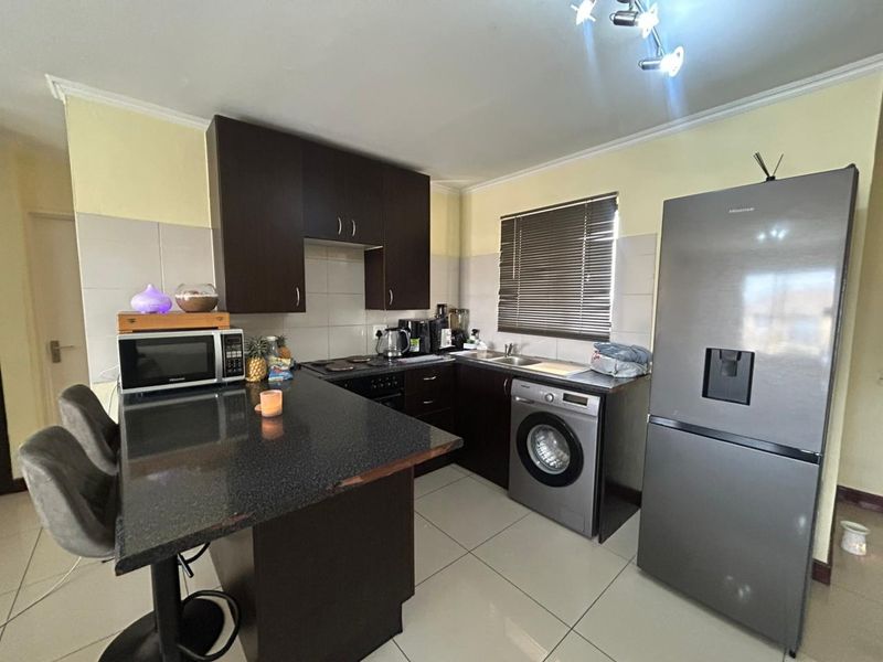 A functional kitchen featuring dark wood cabinetry, granite countertops, a breakfast bar, and integrated stainless steel appliances with tiled flooring.