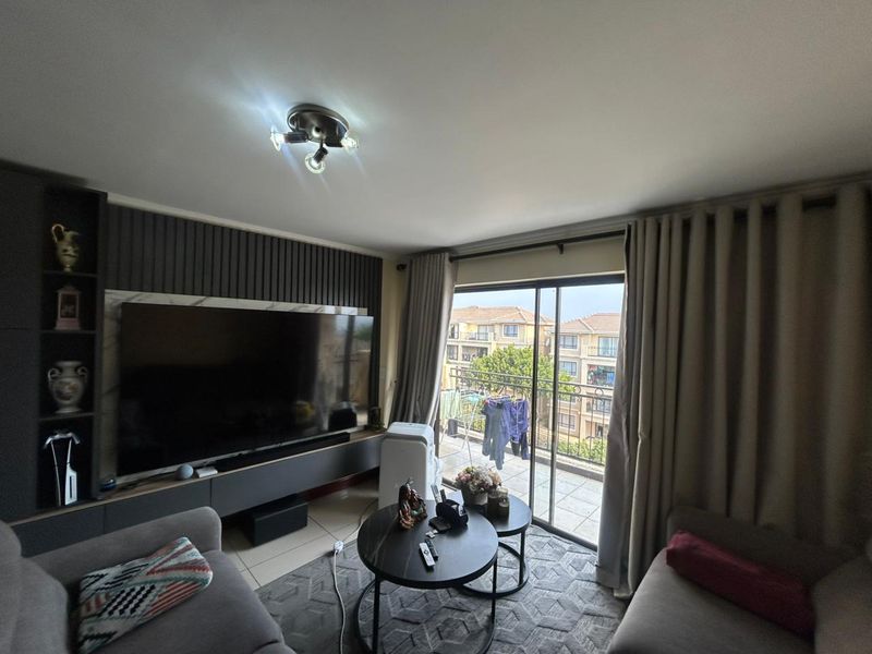 A well-maintained living room featuring a modern built-in media unit with slatted wall detailing and direct access to a private balcony.