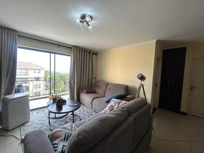 A living room featuring tiled flooring, a ceiling light fixture, and a large sliding glass door providing access to a balcony with exterior views.