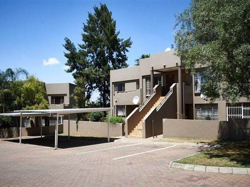 Exterior view of an apartment complex featuring a paved driveway, covered parking bays, and a central staircase leading to the upper level units.