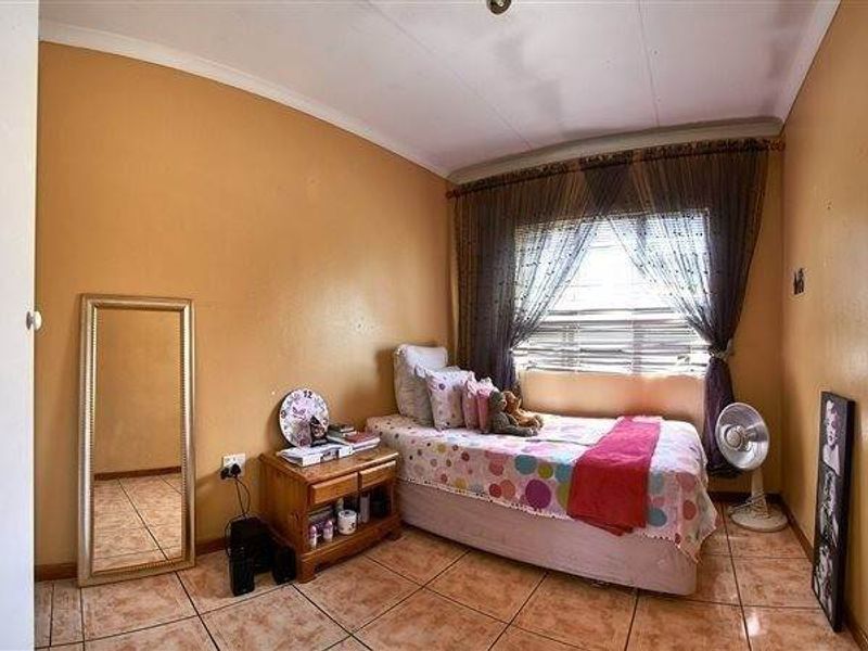 A compact bedroom featuring tiled flooring, a window with curtain treatments, and coved ceiling details, requiring cosmetic updates to improve its overall appeal.