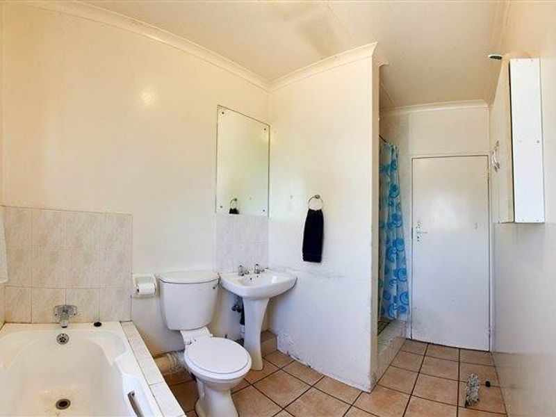 A functional bathroom featuring a bathtub, pedestal sink, toilet, and a separate shower area with tiled flooring and dated finishes.