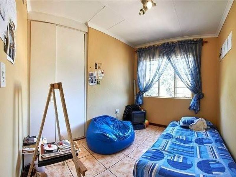 A bedroom featuring tiled flooring, a built-in wardrobe, and a window fitted with security bars.