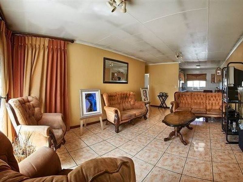 Open plan living area featuring tiled flooring and ceiling panels, with an integrated kitchen visible in the background.