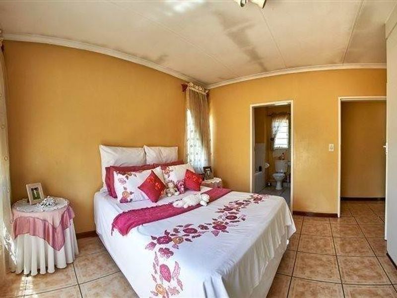 Bedroom featuring tiled flooring and direct access to an en-suite bathroom, with visible signs of ceiling water damage requiring maintenance.