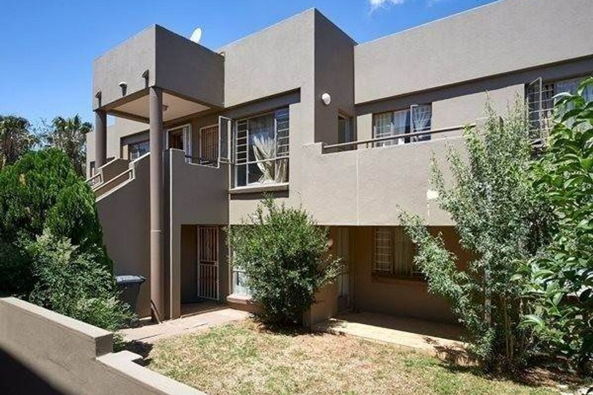 Rear view of a multi-story apartment building featuring a private balcony, ground floor patio area, and established garden space.