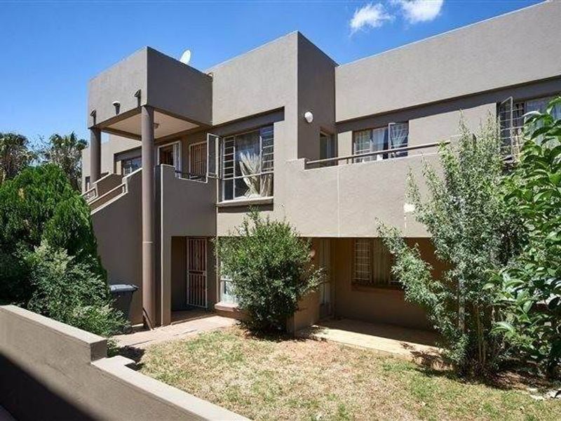 Rear view of a multi-story apartment building featuring a private balcony, ground floor patio area, and established garden space.