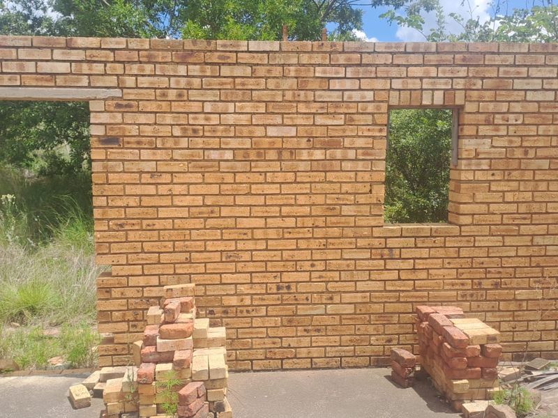 An incomplete face brick wall structure showing a door and window opening, situated on a vacant residential plot.