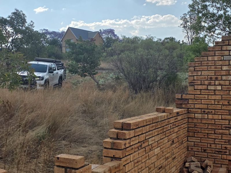 A view of a vacant residential plot featuring an incomplete brick wall structure amidst natural vegetation and surrounding landscape.