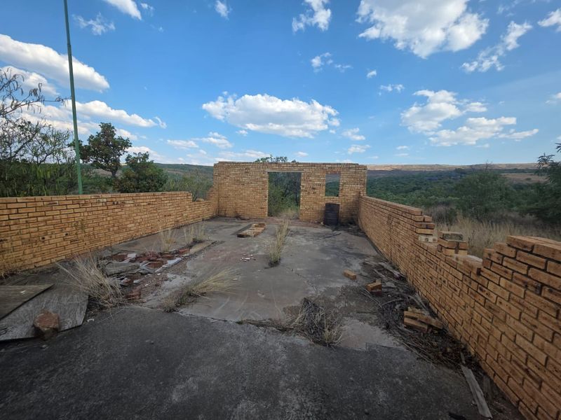 An exterior view of a derelict structure featuring exposed brick walls and a cracked concrete slab foundation on a vacant residential plot.