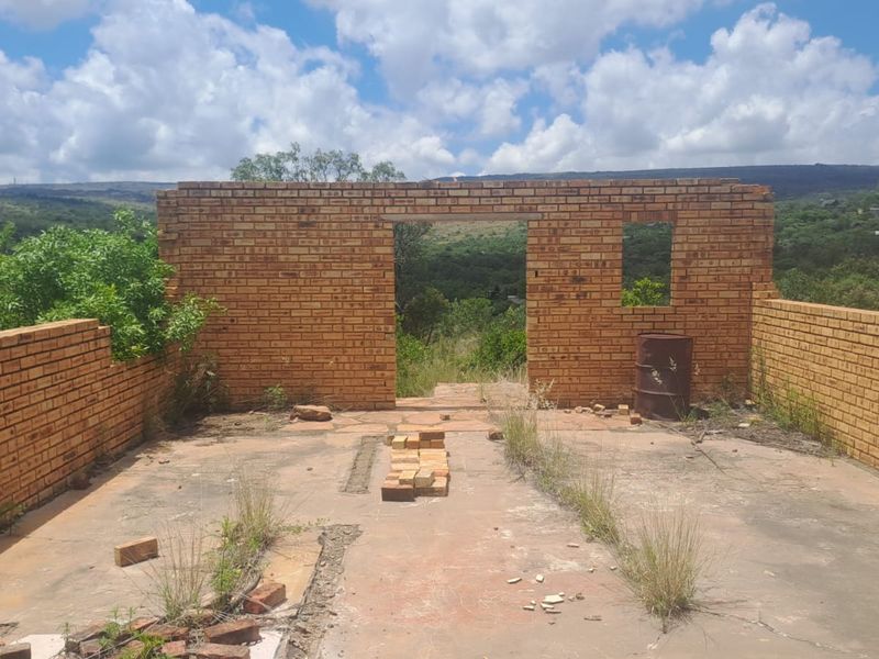 An unfinished brick structure on a vacant residential plot, featuring exposed masonry walls and a concrete slab foundation with scenic landscape views.