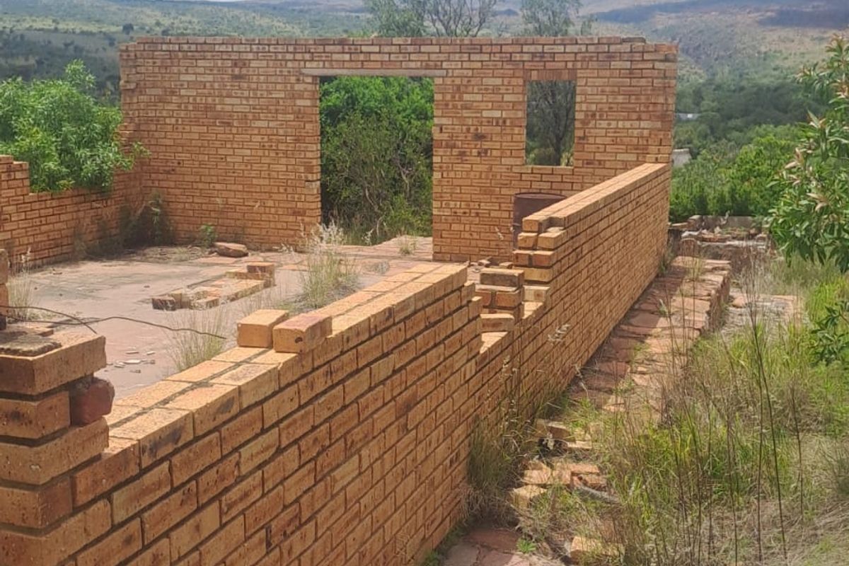 An unfinished brick structure on a residential plot, featuring exposed masonry walls and a concrete slab foundation set within a natural landscape.