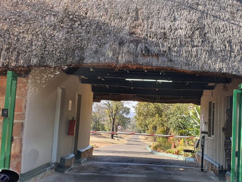Entrance gate to the residential estate featuring a traditional thatch roof, stone cladding, and a security boom gate.
