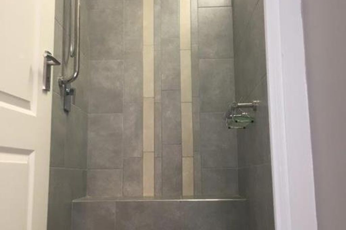 A modern walk-in shower featuring grey and cream wall tiling, a built-in bench, and a mosaic tiled floor.