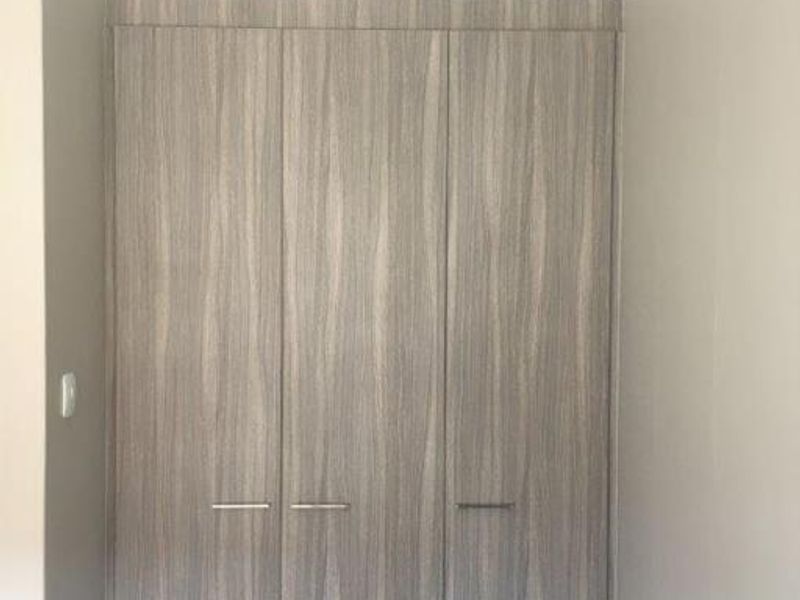 A clean bedroom interior featuring modern, wood-grain finish built-in wardrobes with sleek metal handles and neutral wall tones.