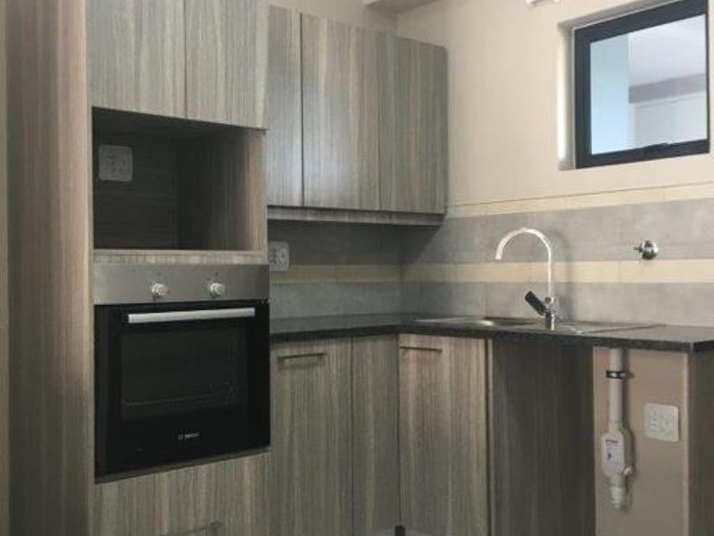 Modern kitchen featuring wood-look laminate cabinetry, built-in oven, stone countertops, and a tiled backsplash with dedicated plumbing for an appliance.