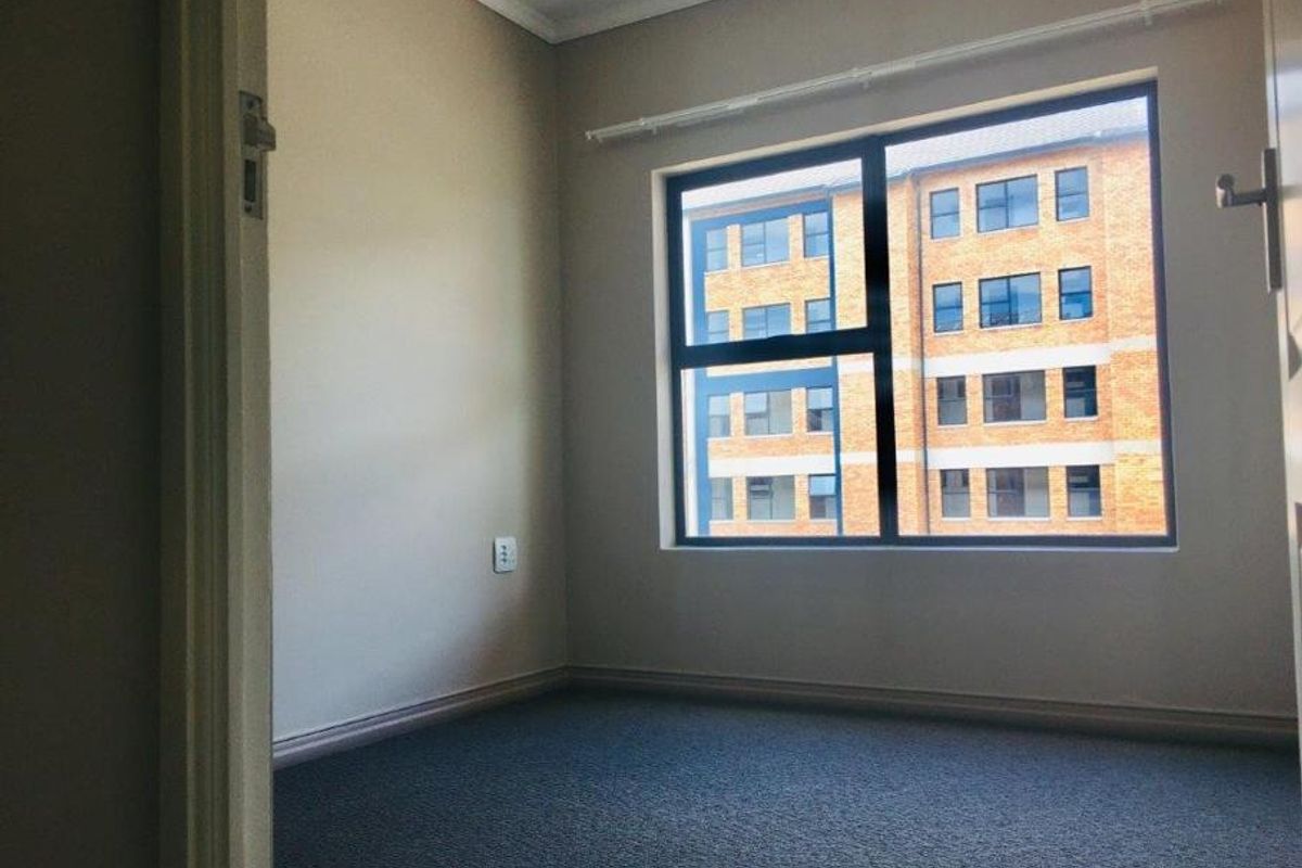 A clean, empty bedroom featuring neutral wall paint, carpeted flooring, and a large window with an aluminium frame.