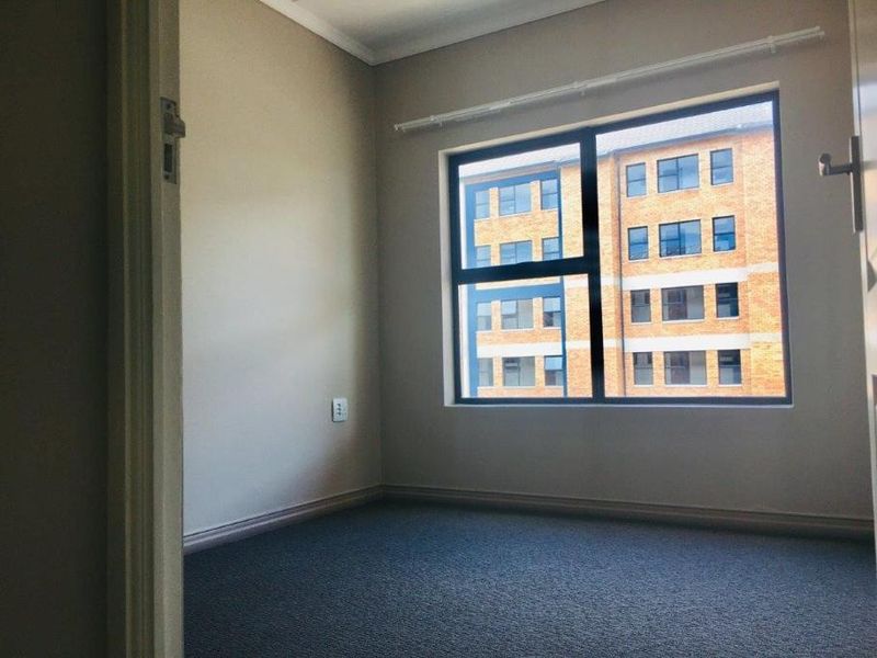 A clean, empty bedroom featuring neutral wall paint, carpeted flooring, and a large window with an aluminium frame.