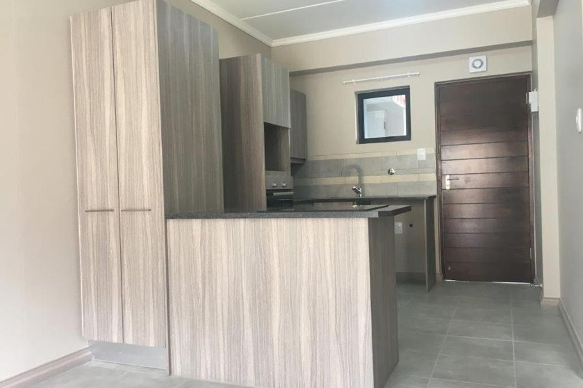 A modern, empty kitchen featuring light wood-grain cabinetry, dark laminate countertops, tiled flooring, and a built-in oven, offering a clean and functional workspace.