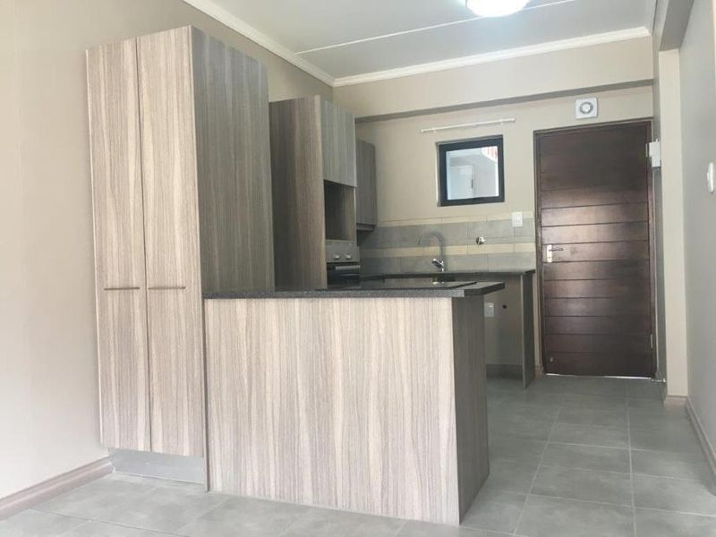 A modern, empty kitchen featuring light wood-grain cabinetry, dark laminate countertops, tiled flooring, and a built-in oven, offering a clean and functional workspace.