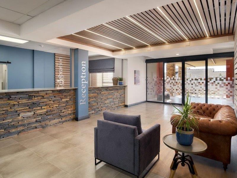 Modern reception area featuring a stone-clad desk, slatted timber ceiling with integrated lighting, and large sliding glass doors leading to an outdoor space.