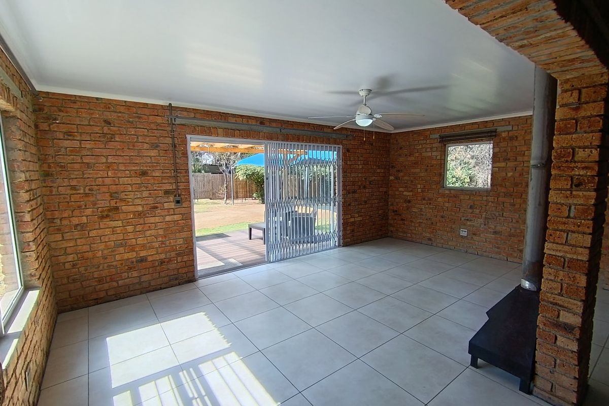 Spacious living area featuring exposed brick walls, tiled flooring, a wood-burning fireplace, and sliding doors providing access to the outdoor patio.