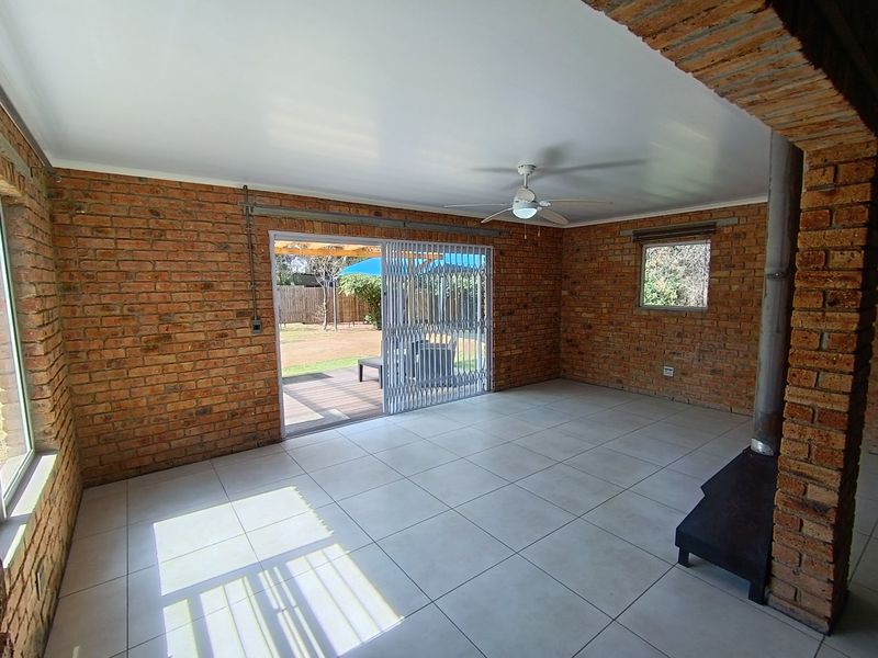 Spacious living area featuring exposed brick walls, tiled flooring, a wood-burning fireplace, and sliding doors providing access to the outdoor patio.