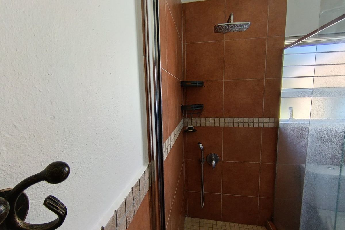 A functional shower enclosure featuring brown wall tiles with a decorative mosaic border, a fixed shower head, and a glass screen.