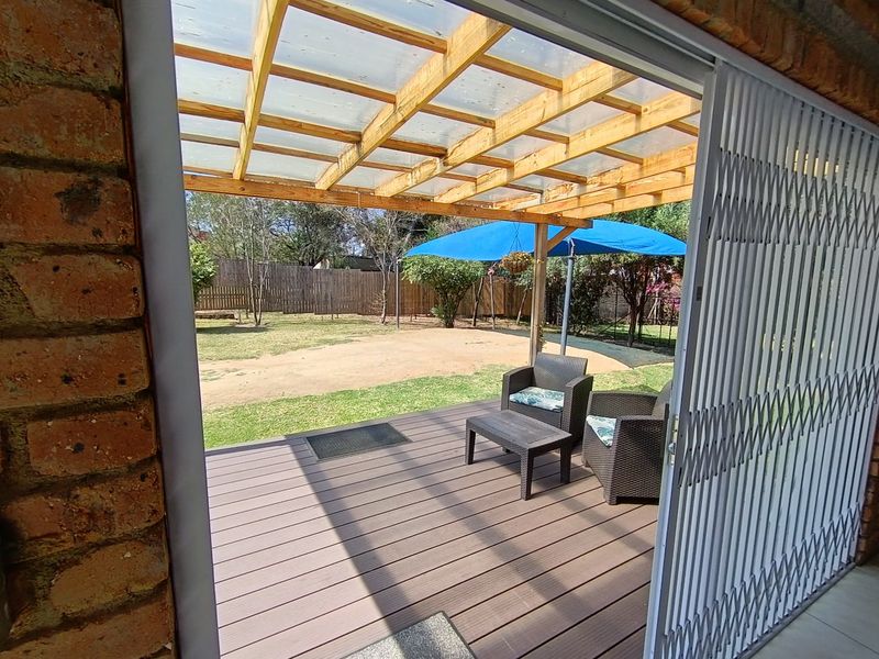 Covered outdoor patio featuring composite decking, a timber pergola with polycarbonate roofing, and a retractable security gate leading to the garden.