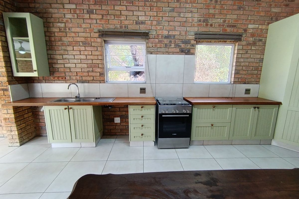 A rustic kitchen featuring exposed brick walls, timber countertops, shaker-style cabinetry, and a freestanding oven, complemented by tiled flooring and natural light.