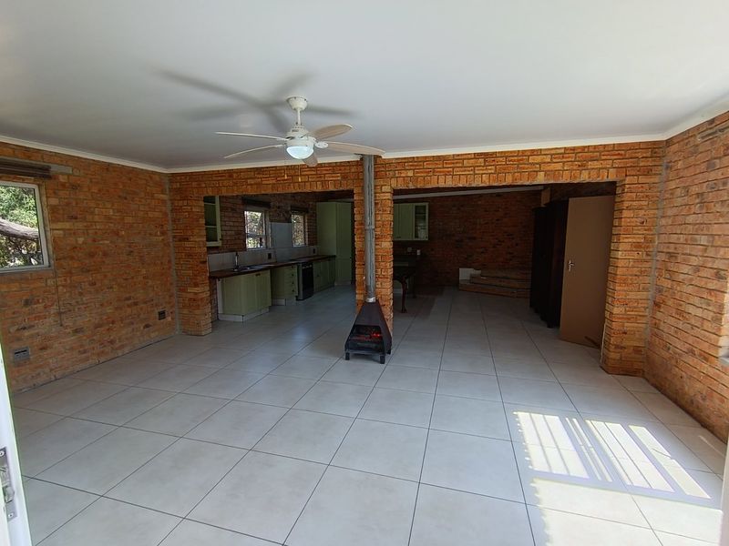 Spacious open-plan living area featuring exposed brick walls, tiled flooring, a central fireplace, and an integrated kitchen with built-in cabinetry.