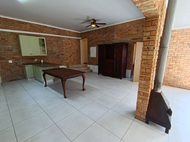 Spacious open-plan living area featuring exposed brick walls, ceramic tile flooring, a built-in kitchen unit, and a characterful brick archway with a fireplace.