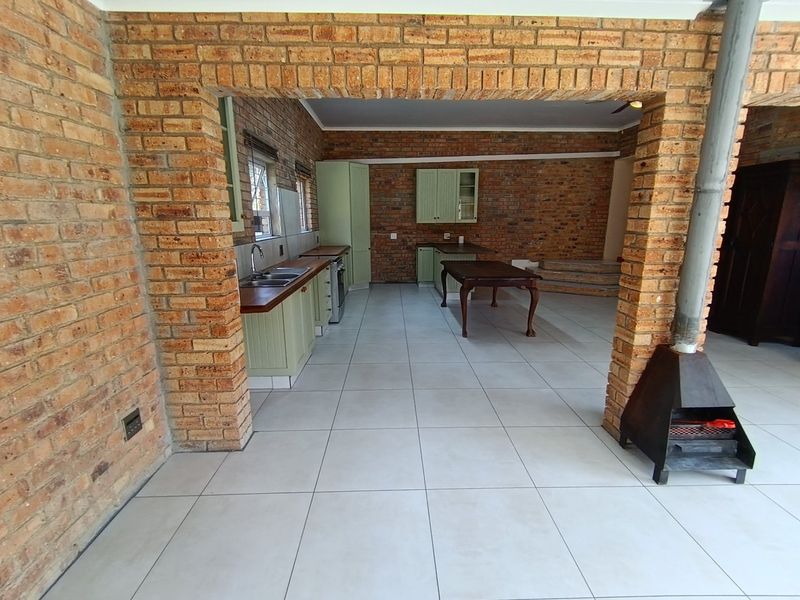 Spacious open-plan kitchen and living area featuring exposed brick walls, tiled flooring, and a central fireplace, offering a rustic and versatile living space.