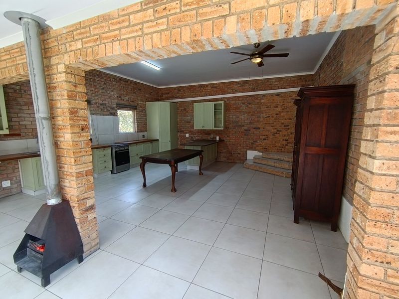 Spacious open-plan kitchen and living area featuring exposed brick walls, tiled flooring, and a central freestanding fireplace.