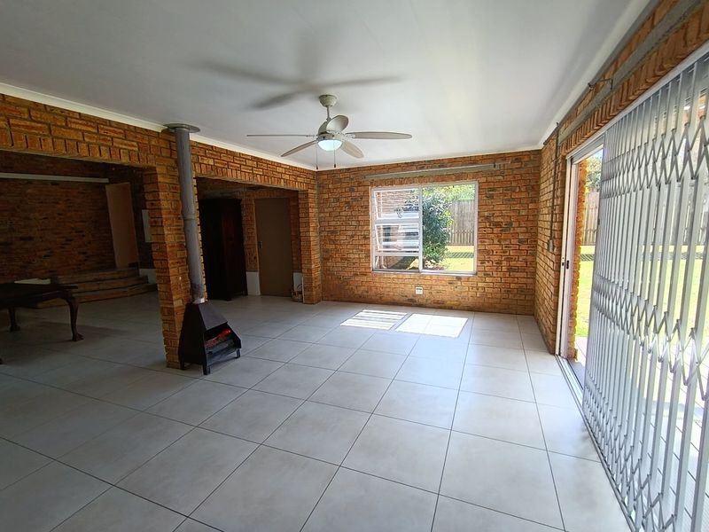 Spacious living area featuring exposed brick walls, tiled flooring, a freestanding fireplace, and direct access to the garden through a sliding glass door.