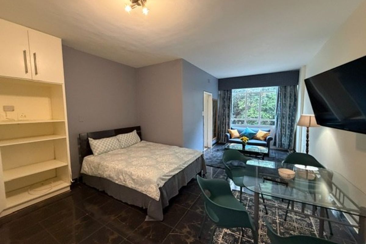 An open-plan studio apartment featuring dark tiled flooring, a built-in storage unit, and a combined living and sleeping area with large window views.