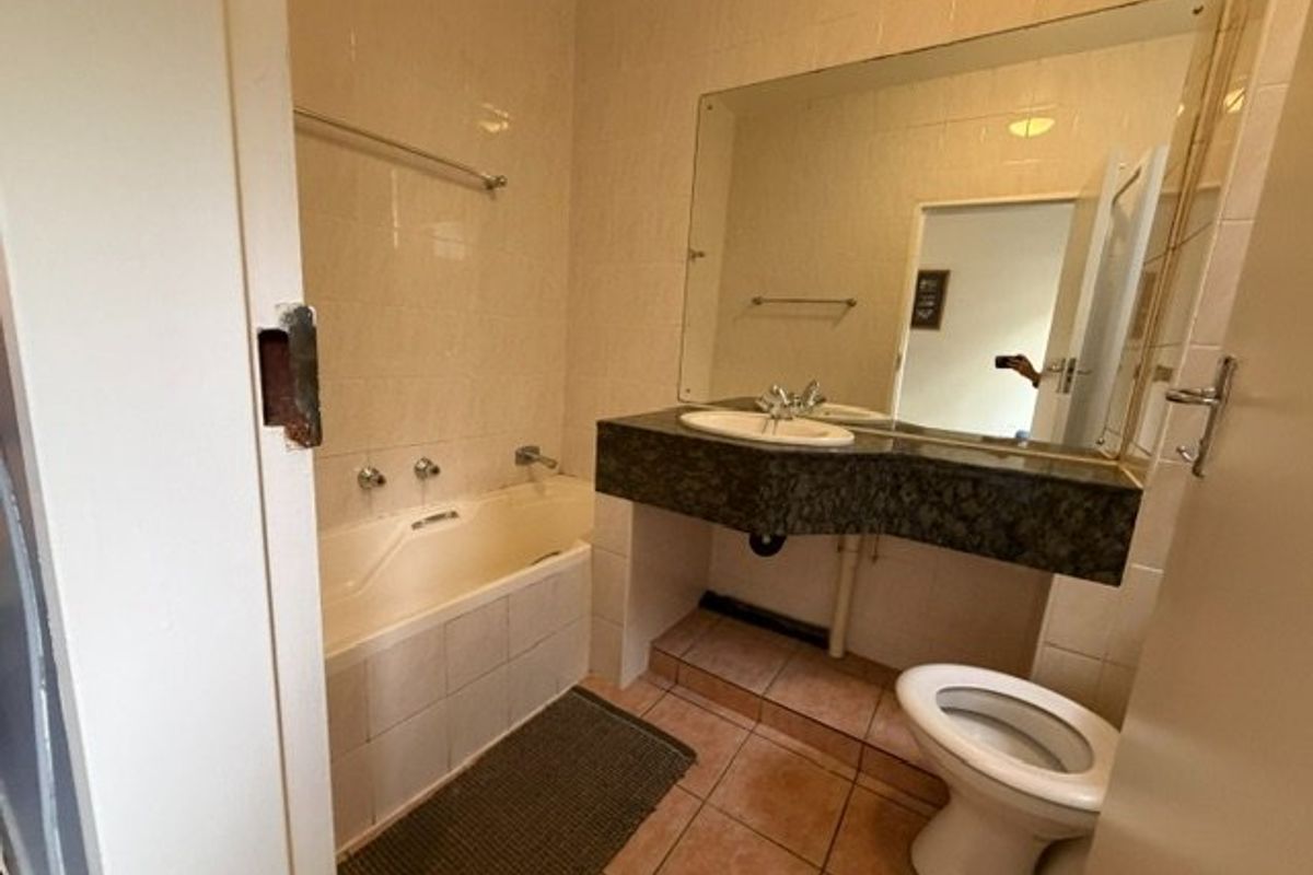 A dated bathroom featuring a bathtub, vanity with stone countertop, and tiled finishes. The space is functional but would benefit from modern updates.
